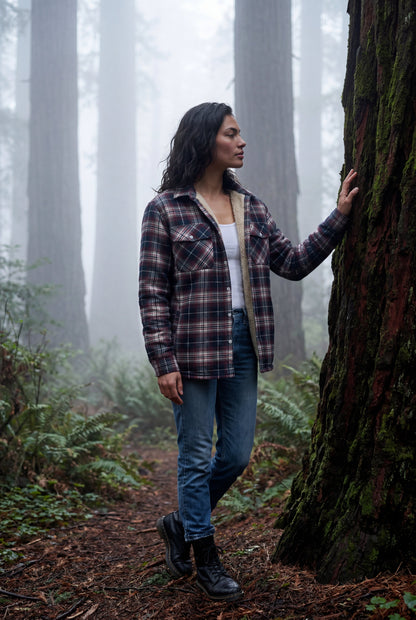 Red - A woman wearing a brown plaid check shirt jacket with a cream-coloured sherpa lining, styled with dark blue slim-fit jeans and brown leather lace-up boots against a plain grey background.