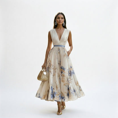 White - A woman wearing a pale green long-sleeve maxi dress with a dark green floral motif, featuring a pleated chiffon texture, V-neckline, and a flowing skirt.