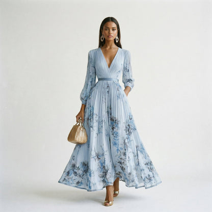 Blue - A woman wearing a pale green long-sleeve maxi dress with a dark green floral motif, featuring a pleated chiffon texture, V-neckline, and a flowing skirt.