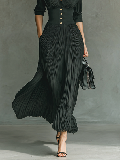 Black - A woman wearing a sophisticated black pleated maxi dress with a structured corset waistband, gold buttons, a spread collar, and elbow-length sleeves.