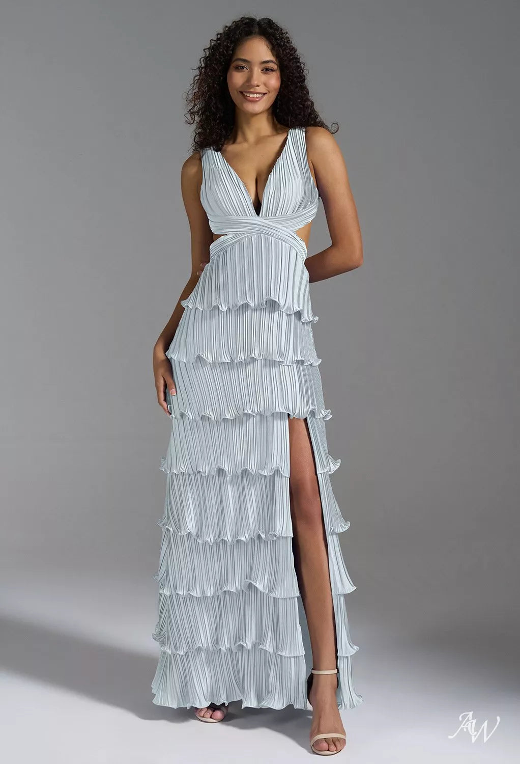 A woman wearing a light blue, floor-length formal dress featuring fine pleating, a plunging V-neckline, waist cut-outs, a tiered skirt, and a high thigh split.