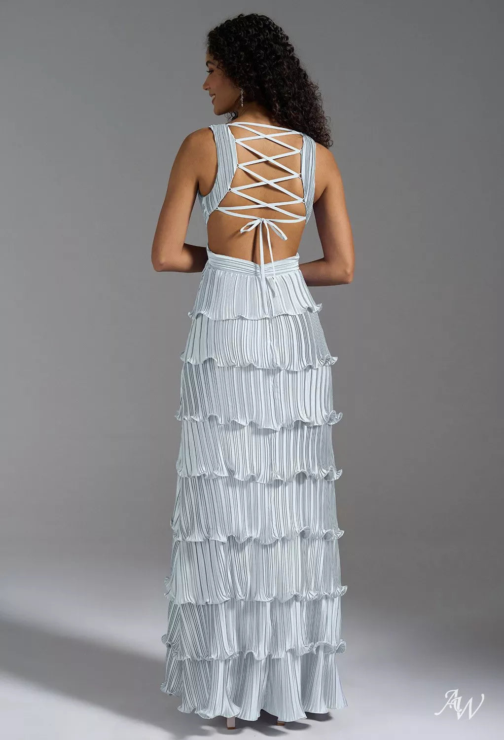 A woman wearing a light blue, floor-length formal dress featuring fine pleating, a plunging V-neckline, waist cut-outs, a tiered skirt, and a high thigh split.