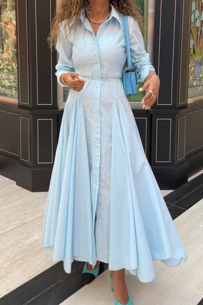 Lake Blue - Woman wearing a light blue, long-sleeved midi shirt dress with a collared neckline, button-front, and a voluminous pleated skirt.