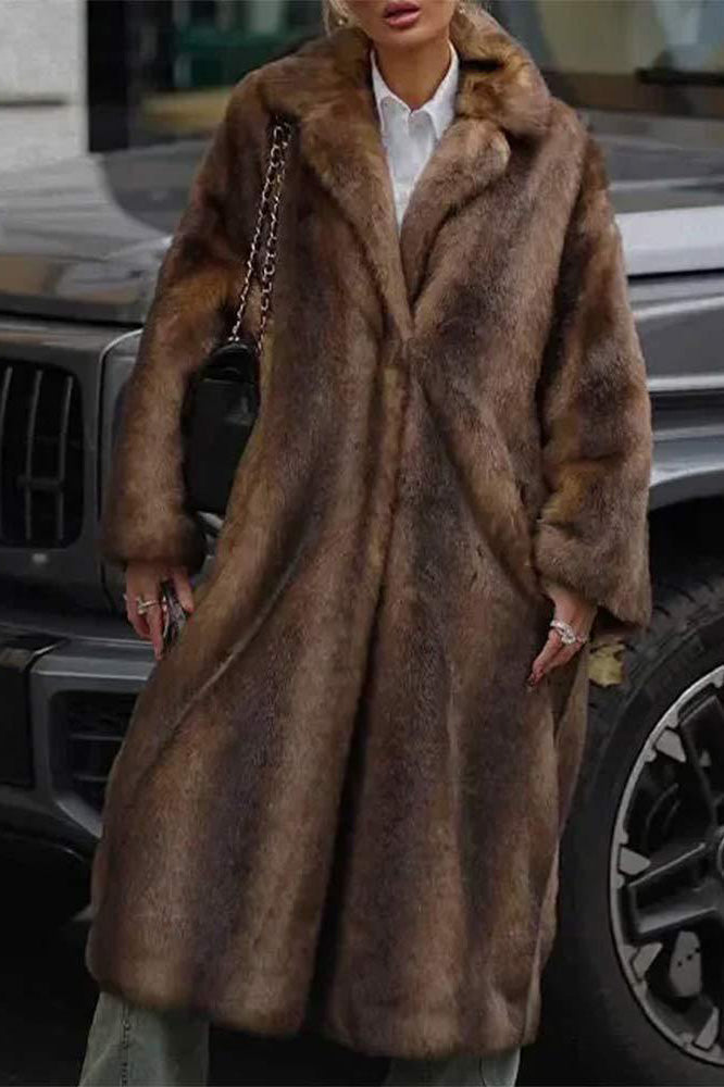 A woman wearing a luxurious, longline brown faux fur coat with oversized lapels, styled over a white collared shirt.