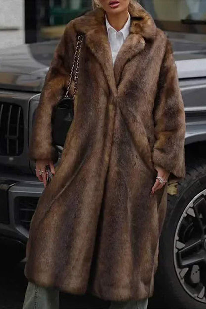 A woman wearing a luxurious, longline brown faux fur coat with oversized lapels, styled over a white collared shirt.