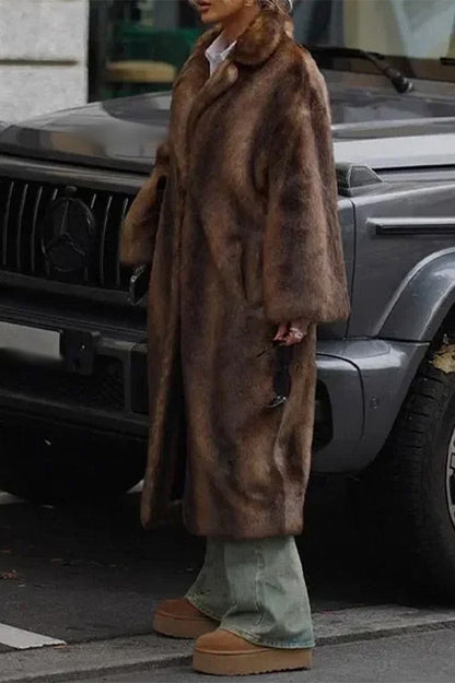 A woman wearing a luxurious, longline brown faux fur coat with oversized lapels, styled over a white collared shirt.