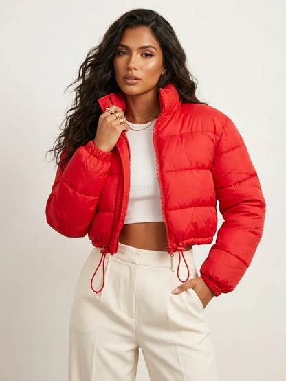 Red - A woman wearing a dark brown cropped puffer jacket with an integrated hood, featuring horizontal quilting, a front zip closure, and adjustable drawstring toggles at the hem, paired with black high-waisted jeans.