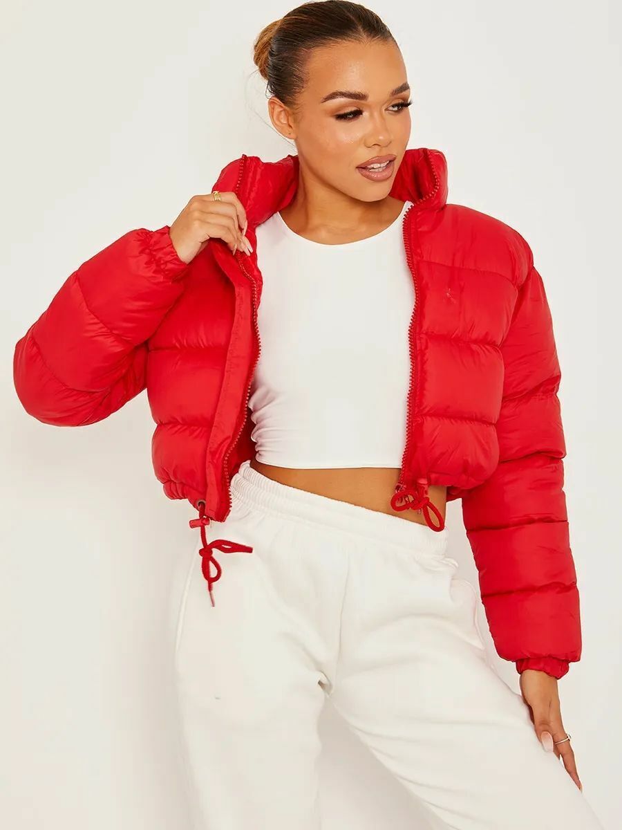 Red - A woman wearing a dark brown cropped puffer jacket with an integrated hood, featuring horizontal quilting, a front zip closure, and adjustable drawstring toggles at the hem, paired with black high-waisted jeans.