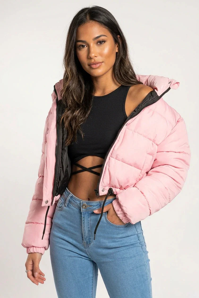Pink - A woman wearing a dark brown cropped puffer jacket with an integrated hood, featuring horizontal quilting, a front zip closure, and adjustable drawstring toggles at the hem, paired with black high-waisted jeans.