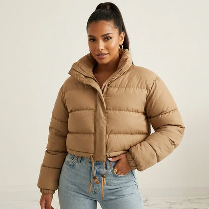 Beige - A woman wearing a dark brown cropped puffer jacket with an integrated hood, featuring horizontal quilting, a front zip closure, and adjustable drawstring toggles at the hem, paired with black high-waisted jeans.