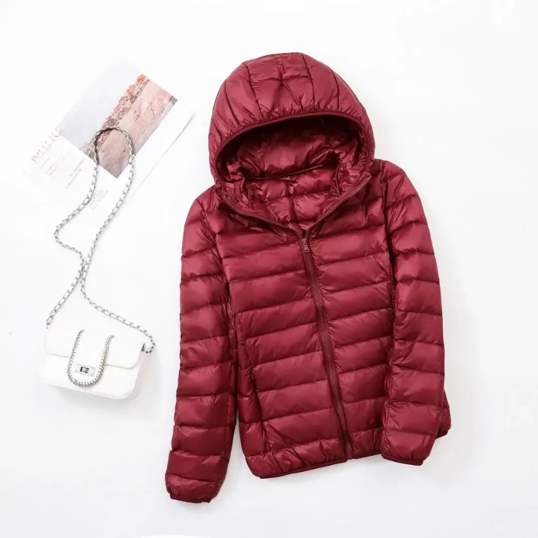 Pink - A woman wearing an off-white hooded puffer jacket with horizontal quilting, zipped up, paired with blue jeans against a plain white background.