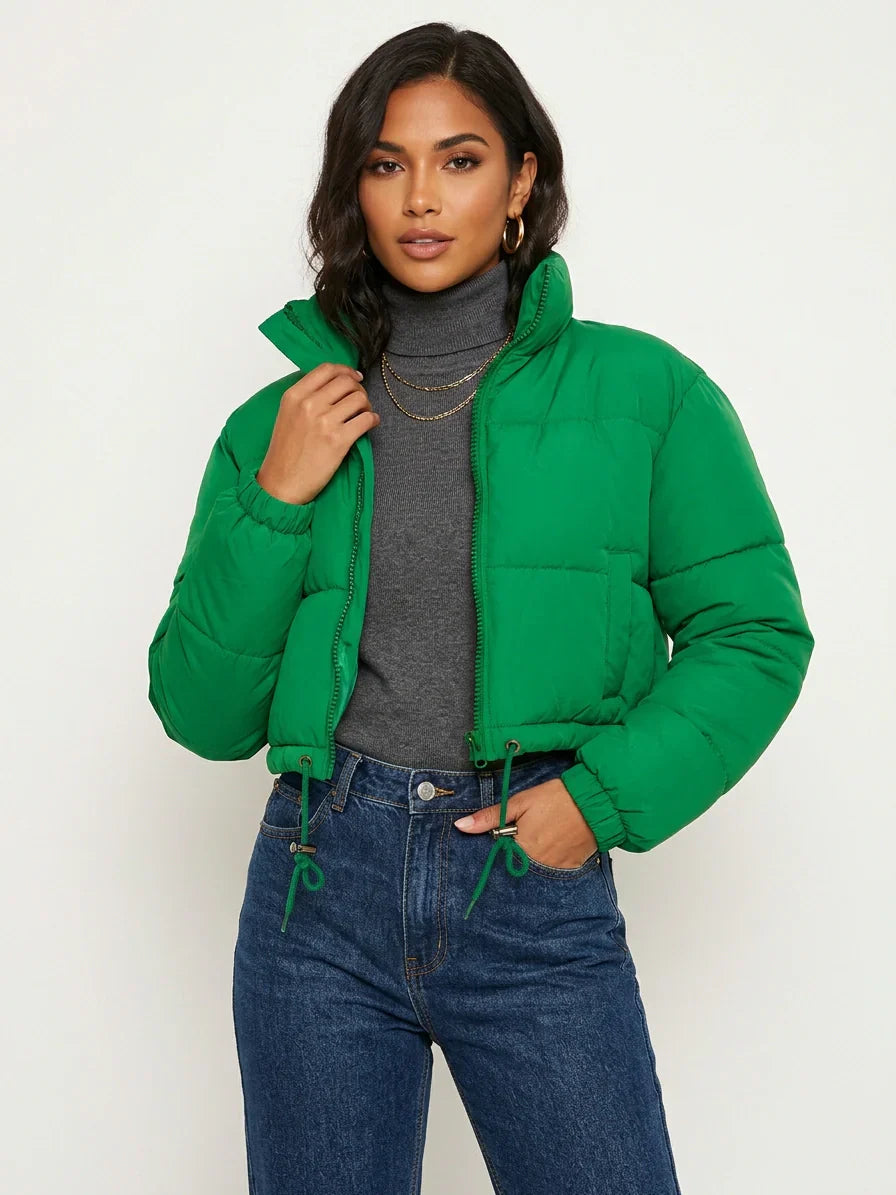 Green - A woman wearing a dark brown cropped puffer jacket with an integrated hood, featuring horizontal quilting, a front zip closure, and adjustable drawstring toggles at the hem, paired with black high-waisted jeans.