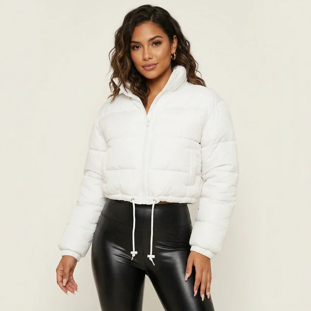 White - A woman wearing a dark brown cropped puffer jacket with an integrated hood, featuring horizontal quilting, a front zip closure, and adjustable drawstring toggles at the hem, paired with black high-waisted jeans.