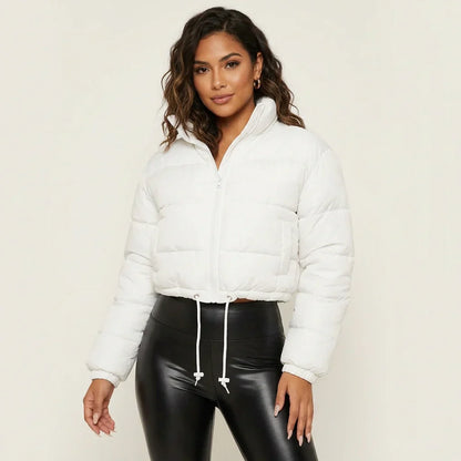 White - A woman wearing a dark brown cropped puffer jacket with an integrated hood, featuring horizontal quilting, a front zip closure, and adjustable drawstring toggles at the hem, paired with black high-waisted jeans.