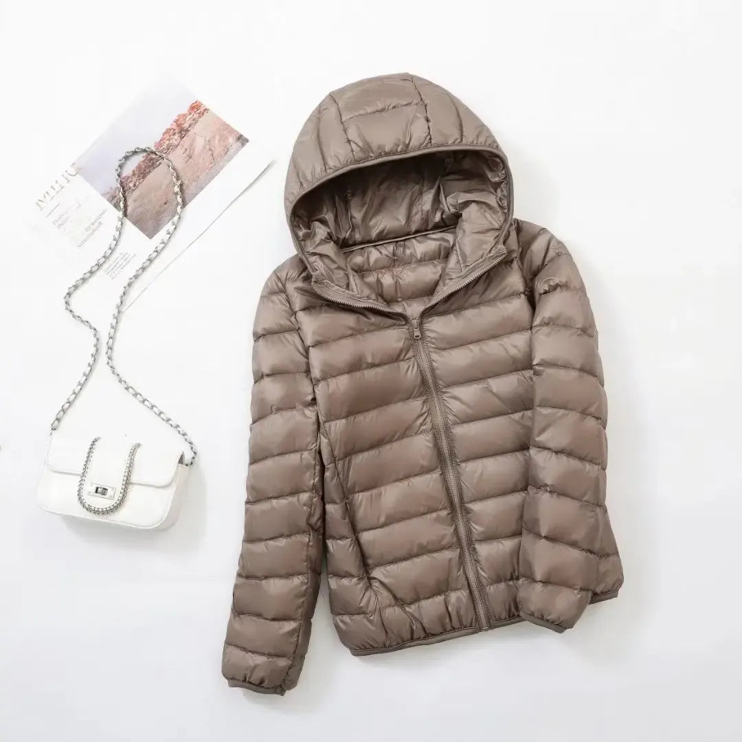 Pink - A woman wearing an off-white hooded puffer jacket with horizontal quilting, zipped up, paired with blue jeans against a plain white background.