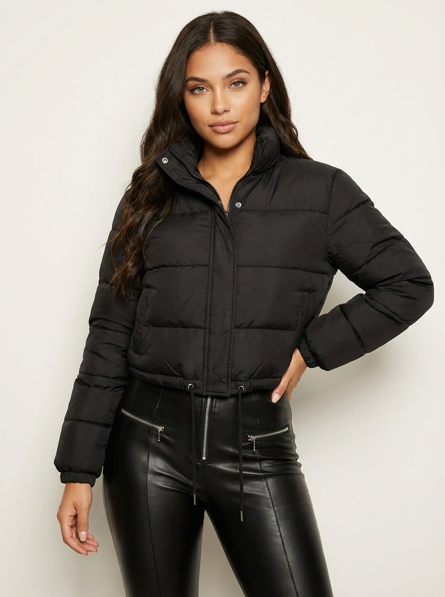 Black - A woman wearing a dark brown cropped puffer jacket with an integrated hood, featuring horizontal quilting, a front zip closure, and adjustable drawstring toggles at the hem, paired with black high-waisted jeans.