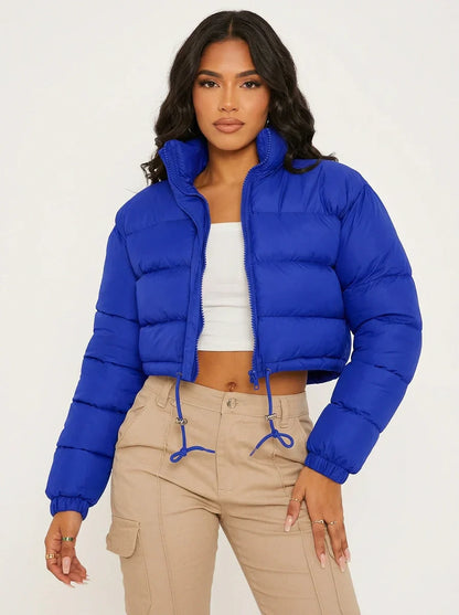 Blue - A woman wearing a dark brown cropped puffer jacket with an integrated hood, featuring horizontal quilting, a front zip closure, and adjustable drawstring toggles at the hem, paired with black high-waisted jeans.
