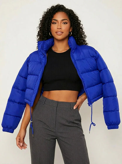 Blue - A woman wearing a dark brown cropped puffer jacket with an integrated hood, featuring horizontal quilting, a front zip closure, and adjustable drawstring toggles at the hem, paired with black high-waisted jeans.