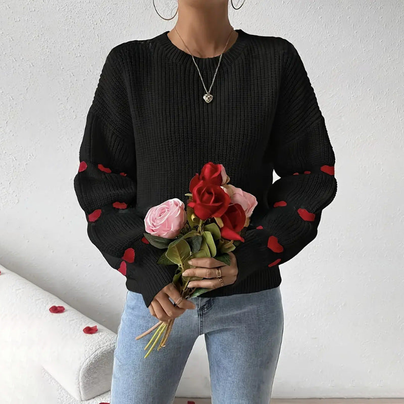 Black - Women's white ribbed knit sweater featuring a crew neckline and long sleeves adorned with horizontal bands of red heart motifs, styled with blue jeans.