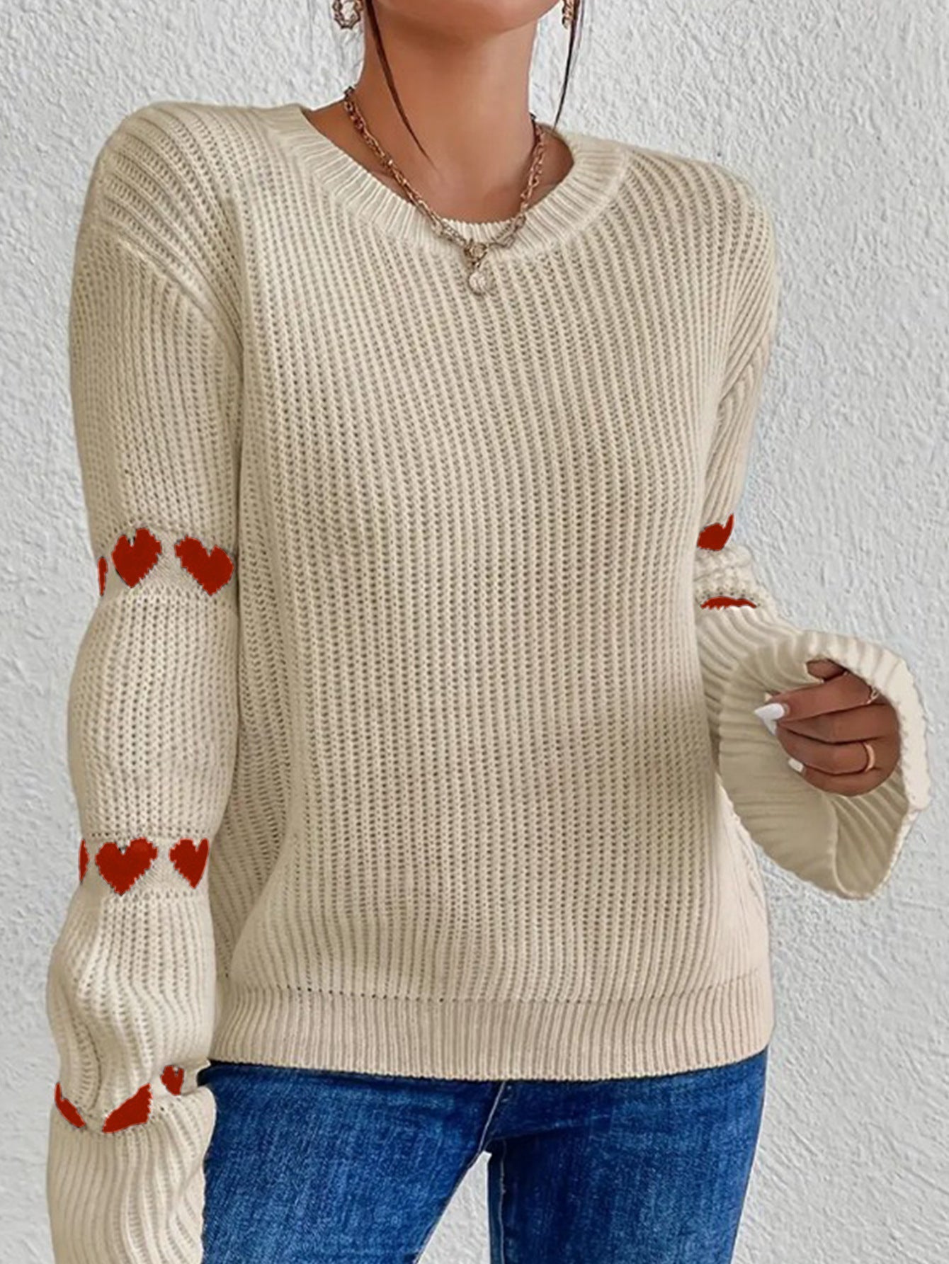 Red Apricot - Women's white ribbed knit sweater featuring a crew neckline and long sleeves adorned with horizontal bands of red heart motifs, styled with blue jeans.