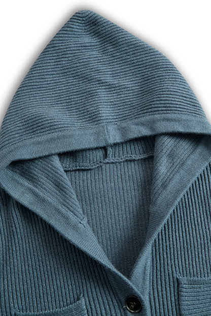 Green - A woman wearing a long-sleeve, blue-grey ribbed knit maxi dress featuring a hood, a button-down neckline, and chest flap pockets, paired with a woven tote bag.