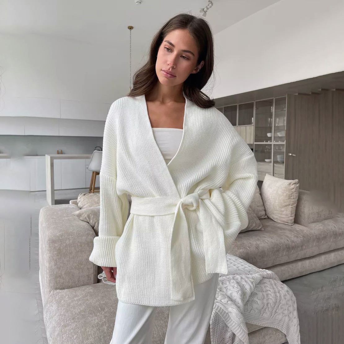 White - A woman wearing a light blue, ribbed knit wrap cardigan featuring a self-tie waist belt and wide folded cuffs, paired with cream trousers against a white background.