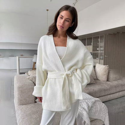 White - A woman wearing a light blue, ribbed knit wrap cardigan featuring a self-tie waist belt and wide folded cuffs, paired with cream trousers against a white background.