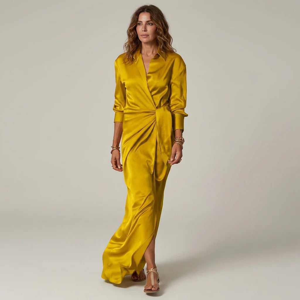 Yellow - A woman wearing a long-sleeve, mustard-yellow satin wrap maxi dress with a collar, tied waist detail, and front split, posing against a neutral grey background.