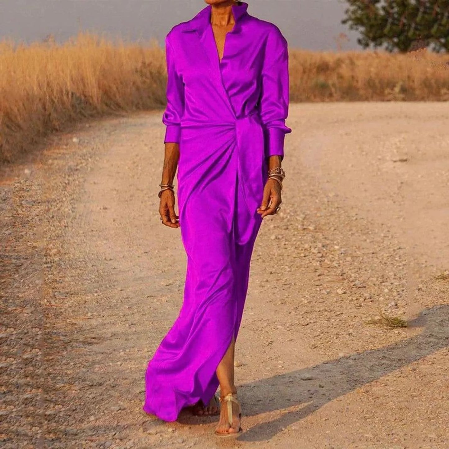 Purple - A woman wearing a long-sleeve, mustard-yellow satin wrap maxi dress with a collar, tied waist detail, and front split, posing against a neutral grey background.
