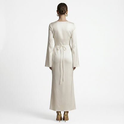 Sand - A woman wearing a long-sleeve chocolate brown satin maxi dress with a round neckline and flared cuffs, standing against a plain white background.