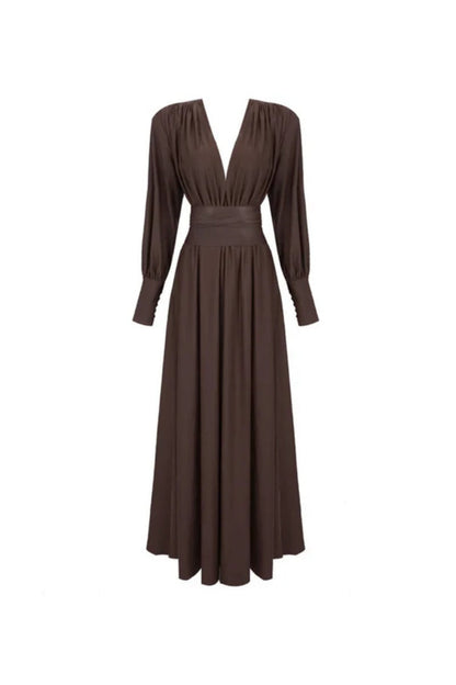 Brown - A woman wearing a chocolate brown satin maxi dress with a plunging V-neckline, ruched bodice, wide structured waist panel, and long bishop sleeves, standing against a city skyline background.