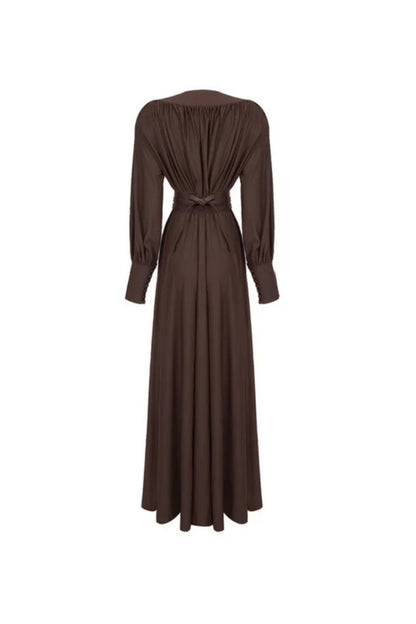 Brown - A woman wearing a chocolate brown satin maxi dress with a plunging V-neckline, ruched bodice, wide structured waist panel, and long bishop sleeves, standing against a city skyline background.