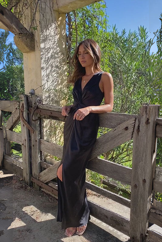 Red - A woman wearing a bronze-coloured satin maxi dress with a plunging V-neckline, twist-front waist detail, and a front split, standing on a rustic stone balcony.