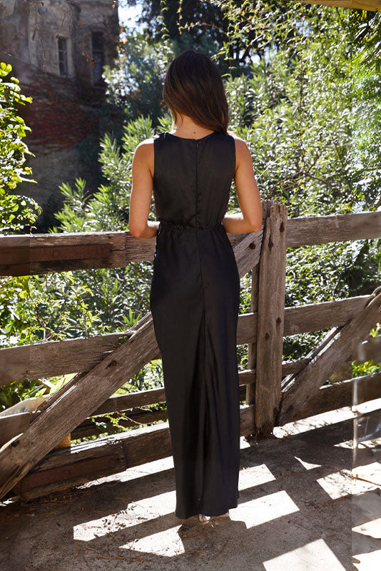 Black - A woman wearing a bronze-coloured satin maxi dress with a plunging V-neckline, twist-front waist detail, and a front split, standing on a rustic stone balcony.