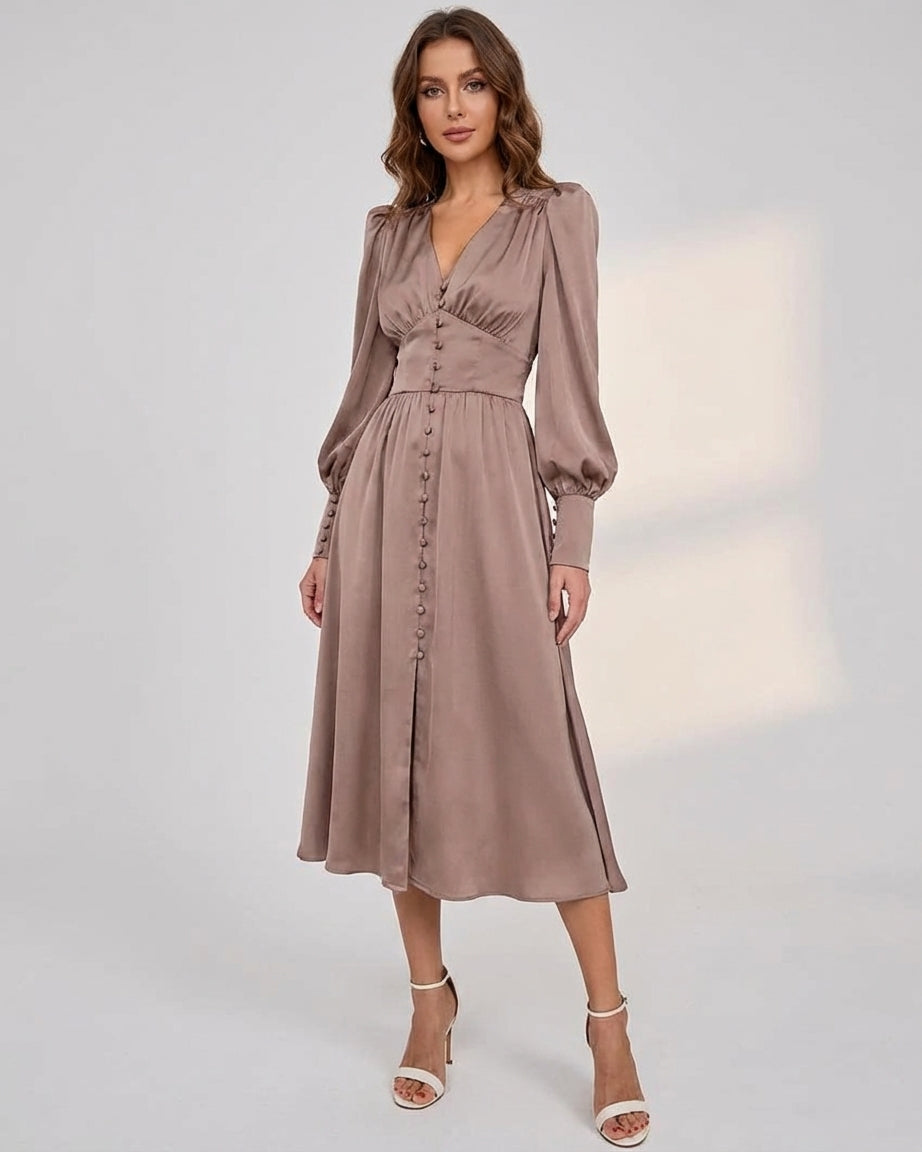A woman wearing a taupe-coloured satin midi dress featuring a V-neckline, a row of self-covered buttons down the front, a cinched waistband, and long bishop sleeves with extended buttoned cuffs.