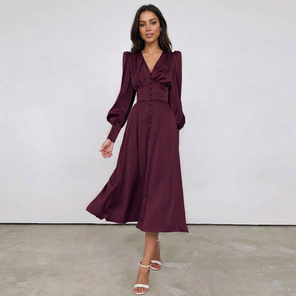 Burgundy - A woman wearing a taupe-coloured satin midi dress featuring a V-neckline, a row of self-covered buttons down the front, a cinched waistband, and long bishop sleeves with extended buttoned cuffs.
