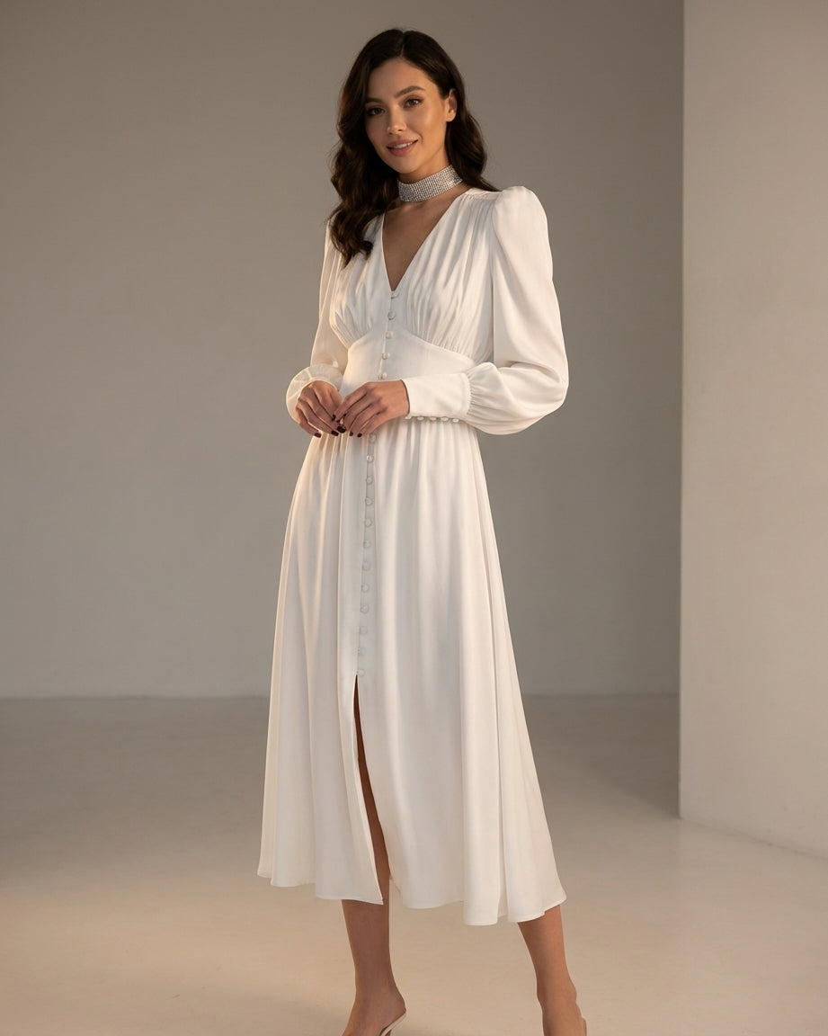 White - A woman wearing a taupe-coloured satin midi dress featuring a V-neckline, a row of self-covered buttons down the front, a cinched waistband, and long bishop sleeves with extended buttoned cuffs.