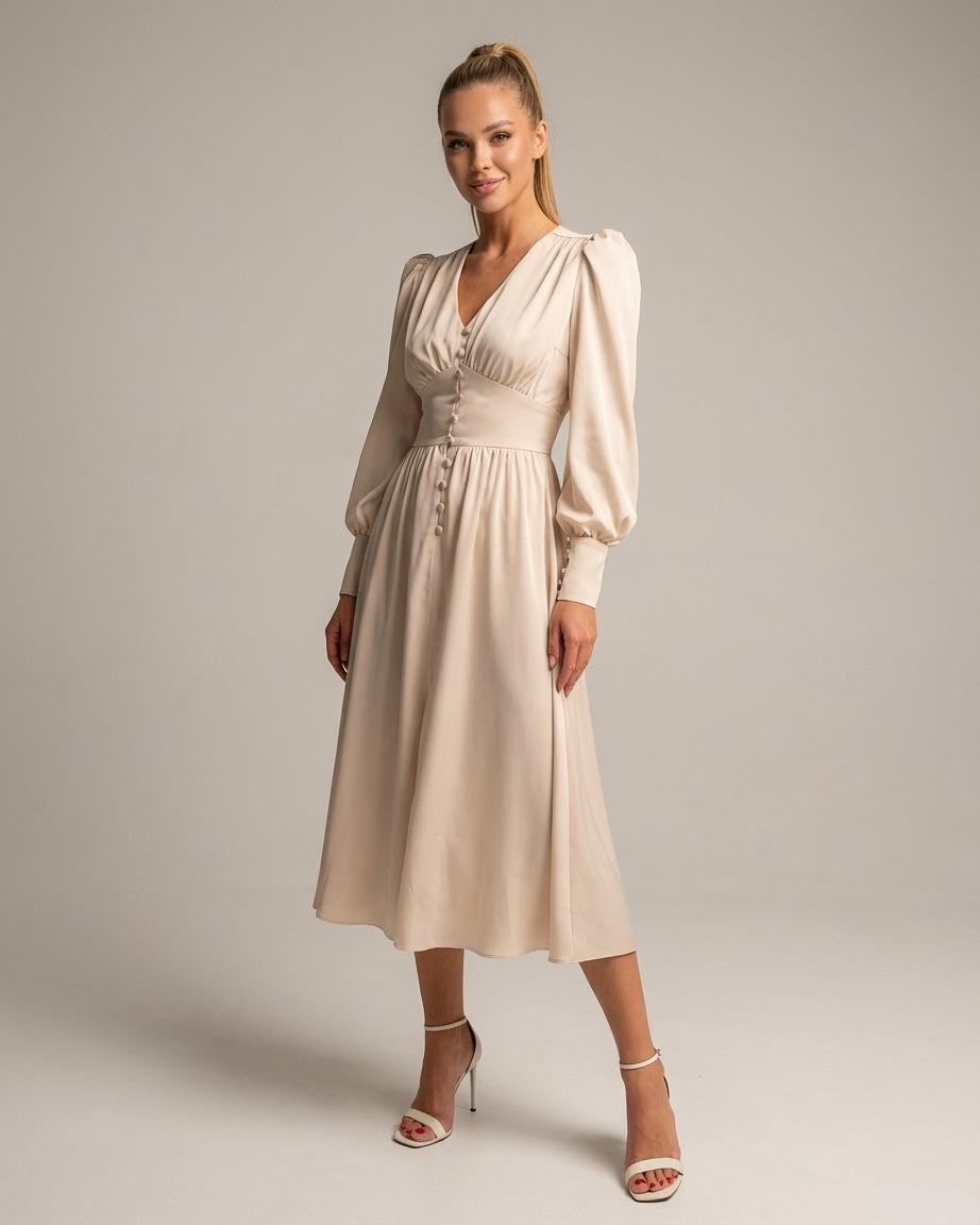 A woman wearing a taupe-coloured satin midi dress featuring a V-neckline, a row of self-covered buttons down the front, a cinched waistband, and long bishop sleeves with extended buttoned cuffs.