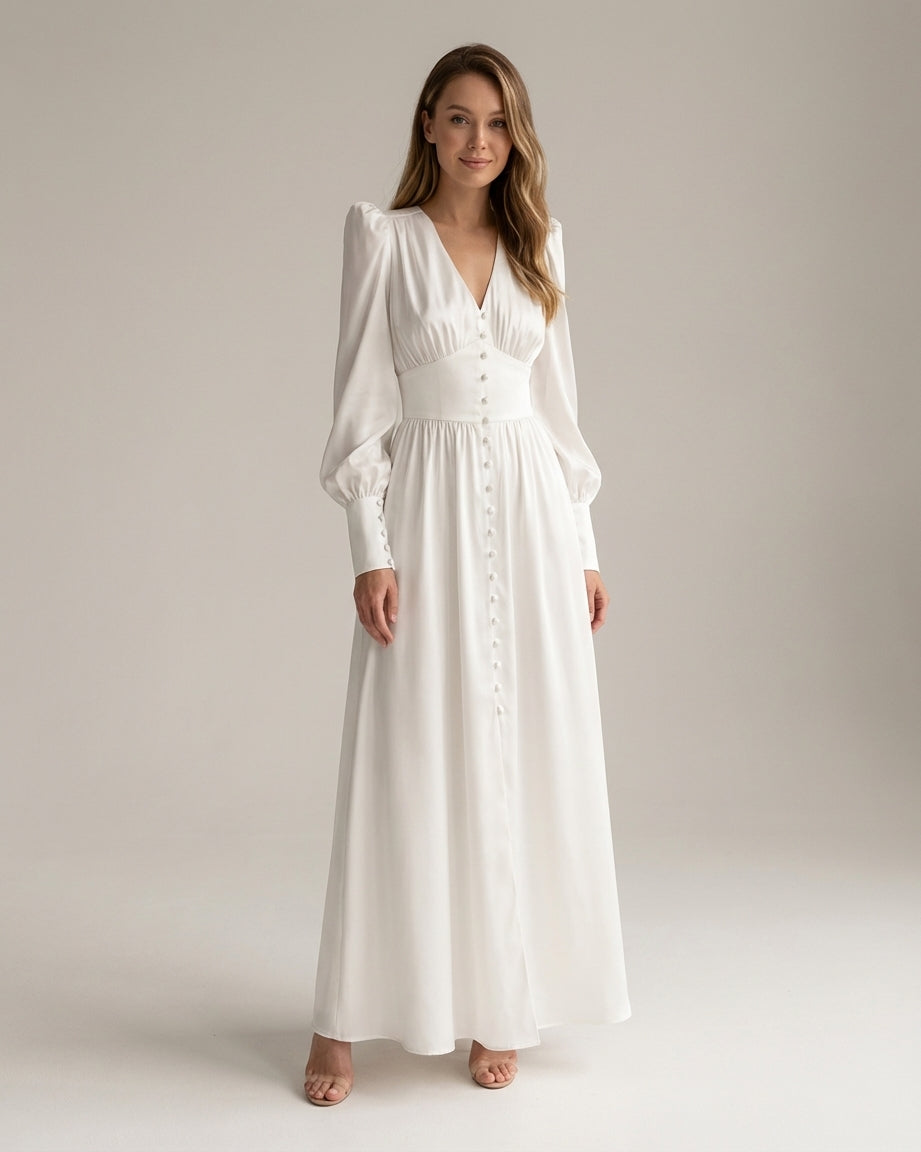 A woman wearing a taupe-coloured satin midi dress featuring a V-neckline, a row of self-covered buttons down the front, a cinched waistband, and long bishop sleeves with extended buttoned cuffs.