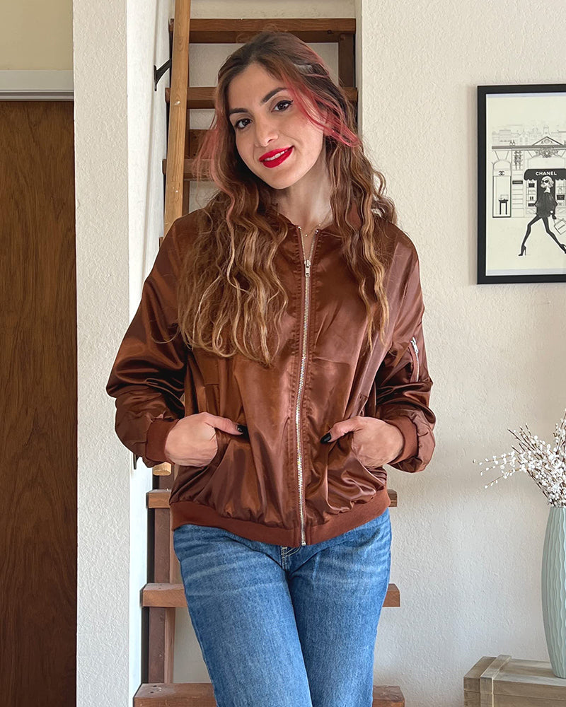Brown - A woman wearing a black, lightweight zip-front bomber jacket with ribbed trims, styled casually open over a t-shirt and denim jeans.