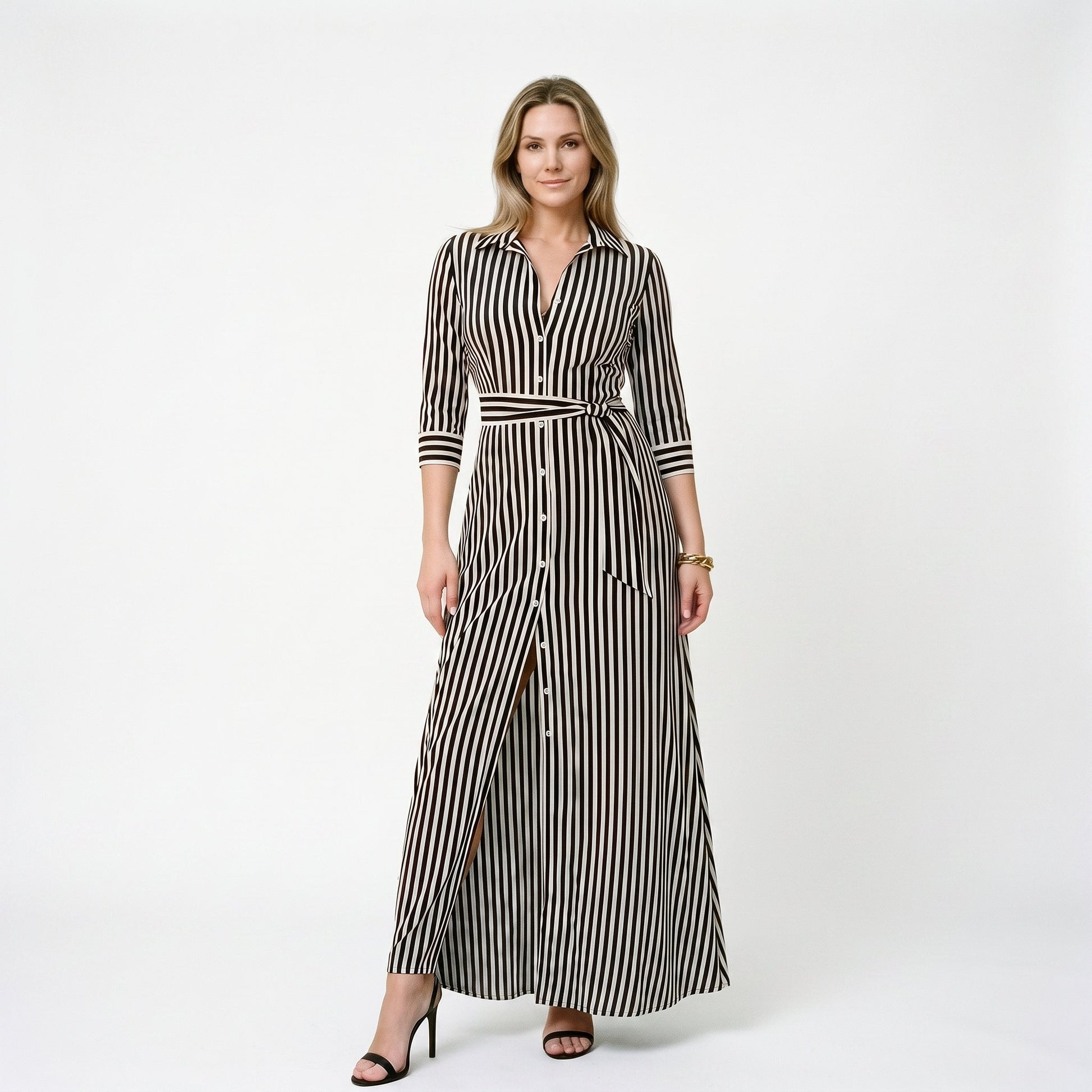Black - A woman wearing a black and white vertically striped maxi shirt dress with a collar, three-quarter sleeves, and a self-tie belt at the waist, paired with black high-heeled sandals against a plain white background.