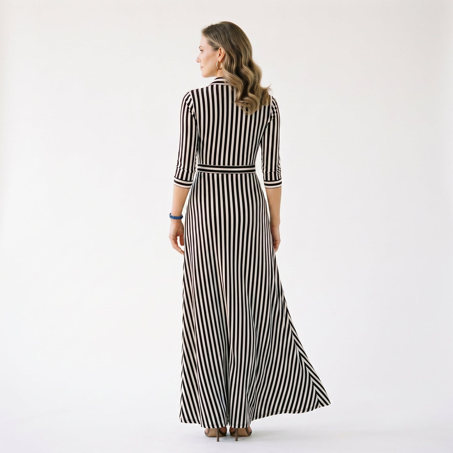 Blue - A woman wearing a black and white vertically striped maxi shirt dress with a collar, three-quarter sleeves, and a self-tie belt at the waist, paired with black high-heeled sandals against a plain white background.