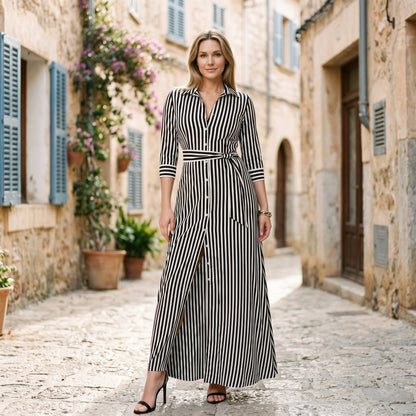 Blue - A woman wearing a black and white vertically striped maxi shirt dress with a collar, three-quarter sleeves, and a self-tie belt at the waist, paired with black high-heeled sandals against a plain white background.