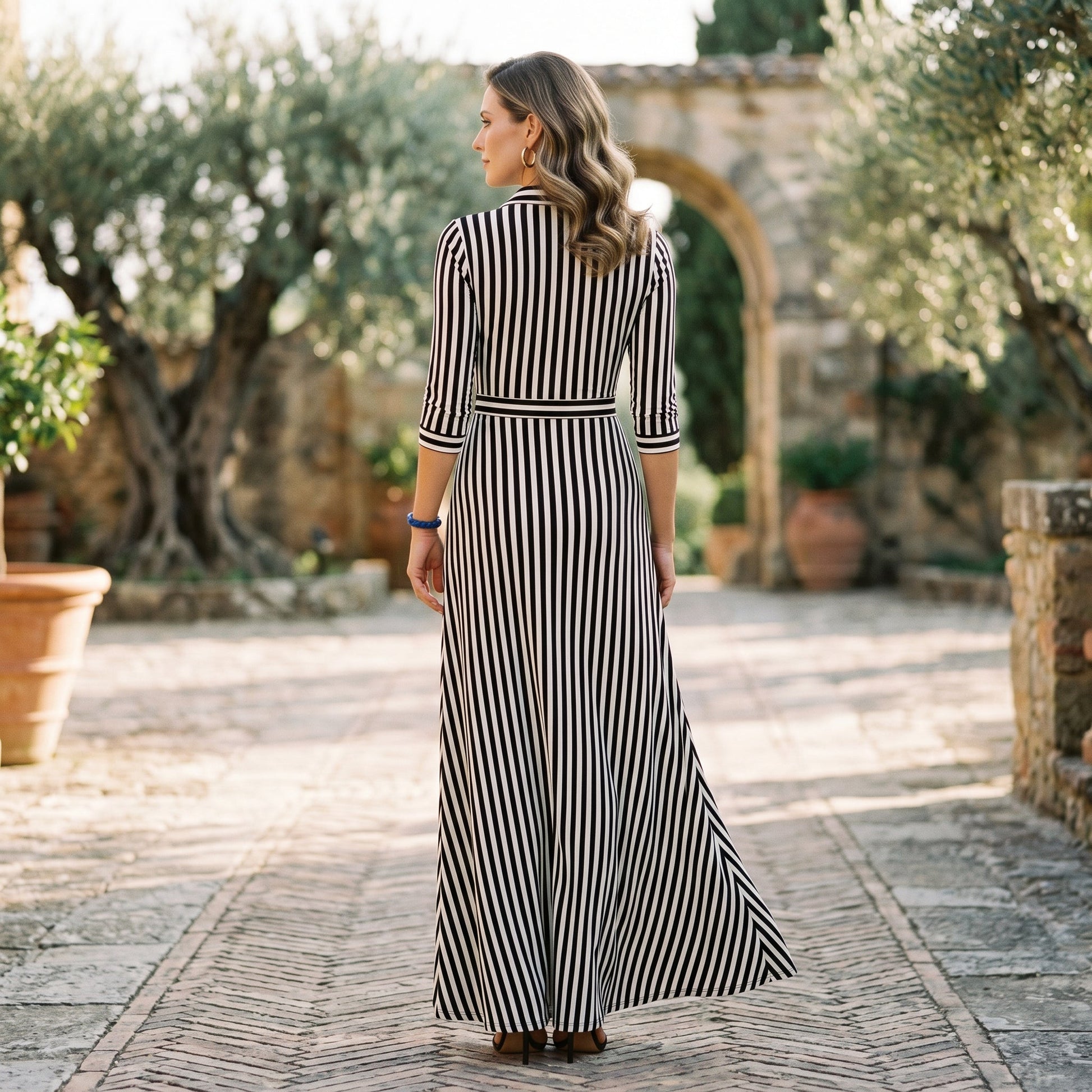 Blue - A woman wearing a black and white vertically striped maxi shirt dress with a collar, three-quarter sleeves, and a self-tie belt at the waist, paired with black high-heeled sandals against a plain white background.