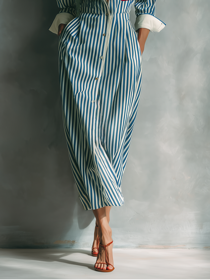 Black And White - A woman wearing a blue and white vertically striped cotton maxi shirt dress with a contrasting red chest pocket, pointed collar, button-down front, and rolled-up white cuffs.