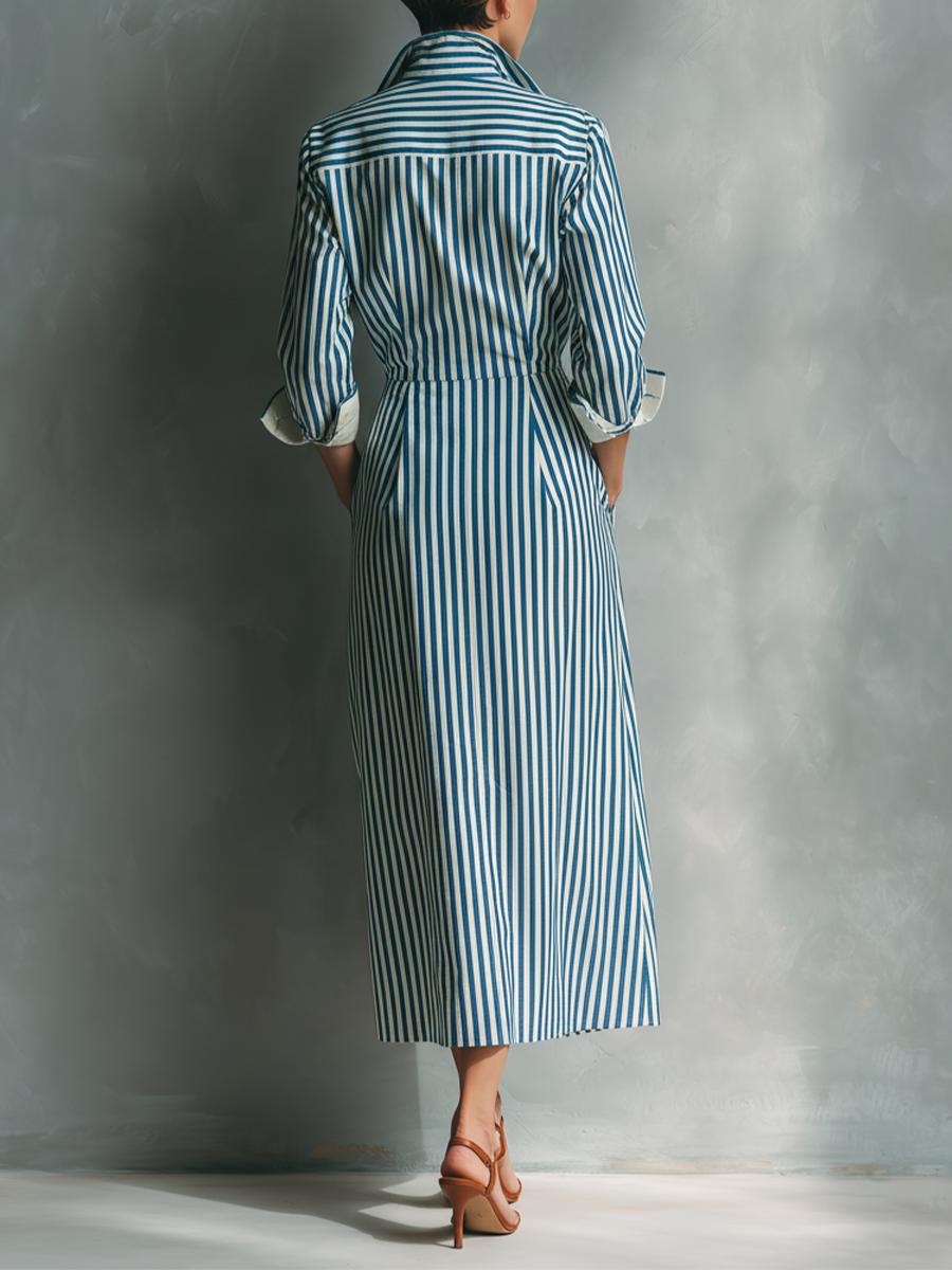 Black And White - A woman wearing a blue and white vertically striped cotton maxi shirt dress with a contrasting red chest pocket, pointed collar, button-down front, and rolled-up white cuffs.