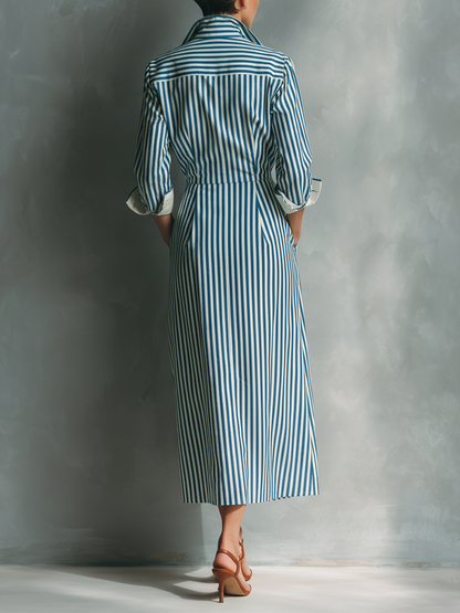 Black And White - A woman wearing a blue and white vertically striped cotton maxi shirt dress with a contrasting red chest pocket, pointed collar, button-down front, and rolled-up white cuffs.