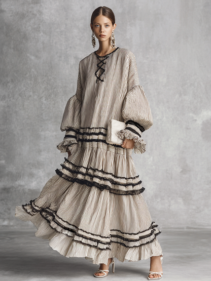 brown and white - A model wearing a voluminous, long-sleeved tiered maxi dress featuring vertical stripes, a lace-up neckline, balloon sleeves, and black ruffled trim along the tiers.