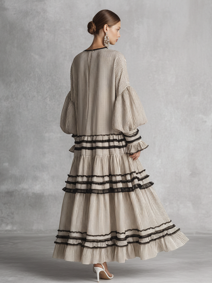 brown and white - A model wearing a voluminous, long-sleeved tiered maxi dress featuring vertical stripes, a lace-up neckline, balloon sleeves, and black ruffled trim along the tiers.