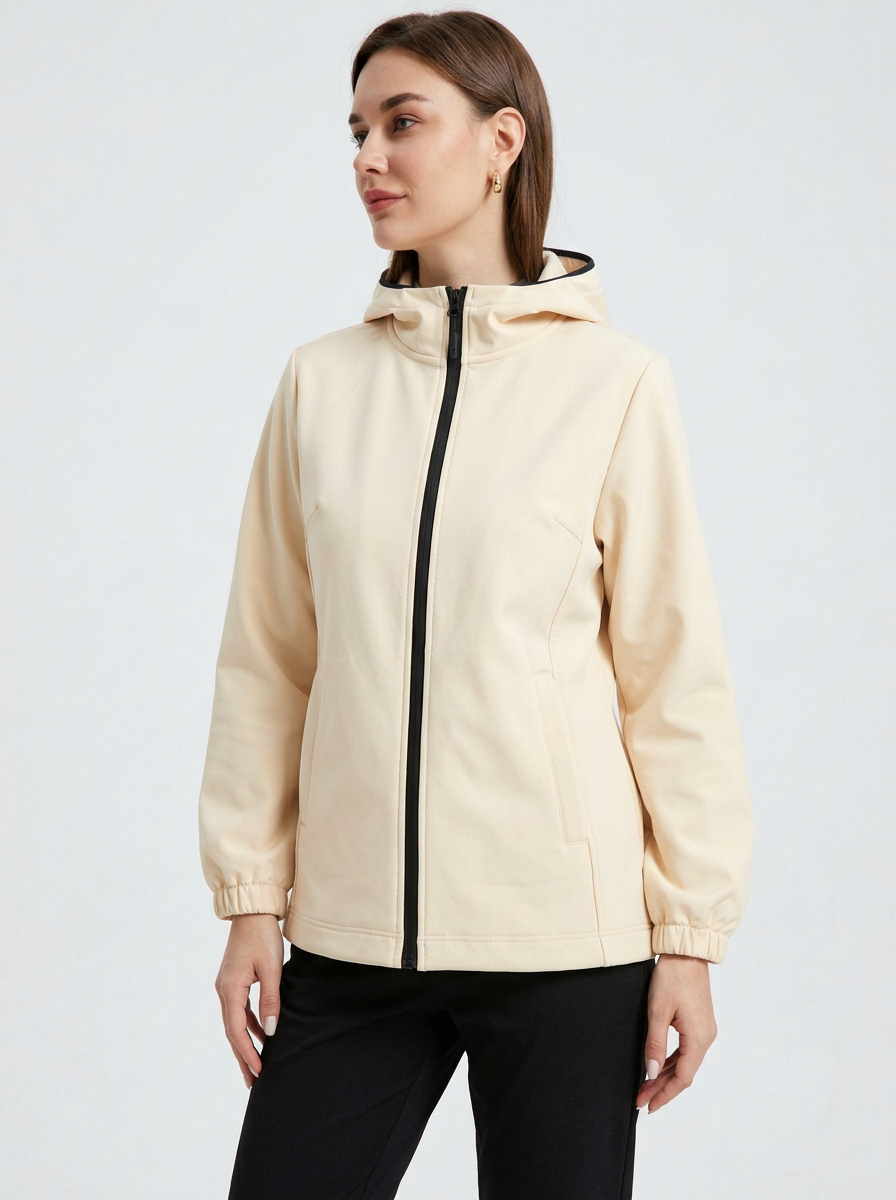 White - A woman wearing a cream-coloured structured hooded jacket with a contrast black front zipper, elasticised cuffs, and side pockets, paired with black pants.